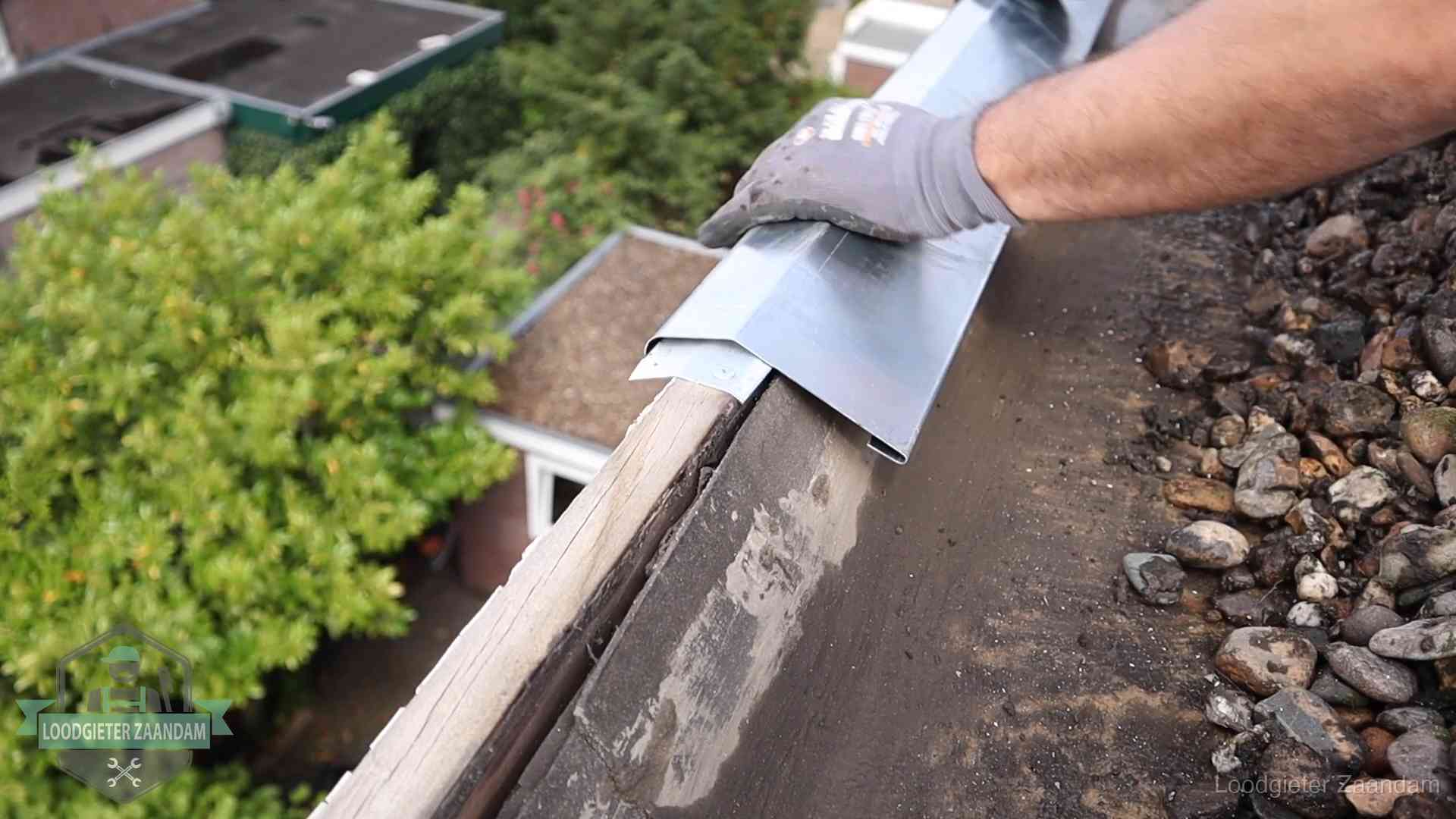 Daklekkage per wijk in Zaandam Dakdekker plaatst een zinken deklijst op een dakrand met uitzicht over een woonwijk in Zaandam