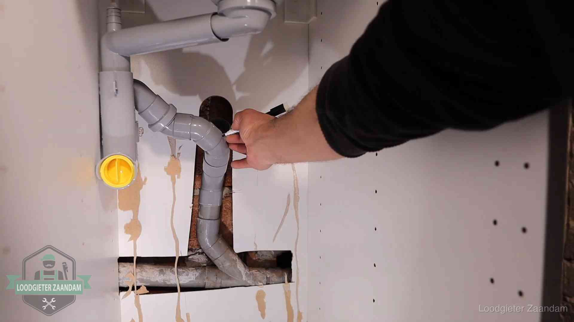 Loodgieter voor verhuurders en bedrijven in Zaandam Loodgieter markeert een pvc-afvoerbuis onder een gootsteen in Zaandam