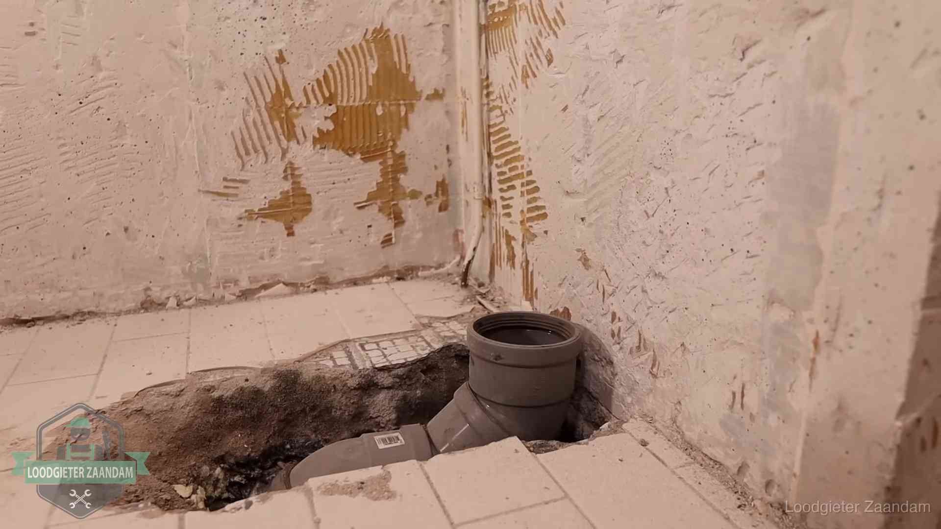 Verzakt riool herstellen in Zaandam Opengebroken vloer met een nieuwe pvc-rioolbocht in een gegraven sleuf in Zaandam