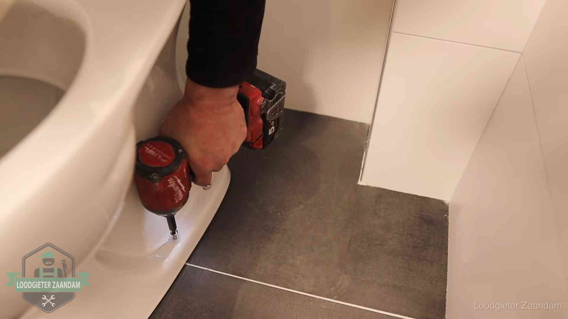 Loodgieter zet de voet van een wc-pot vast op de tegelvloer in Zaandam